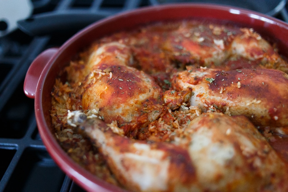 One pot chicken and rice: A red Dutch oven, with red coloured rice and chicken on top.