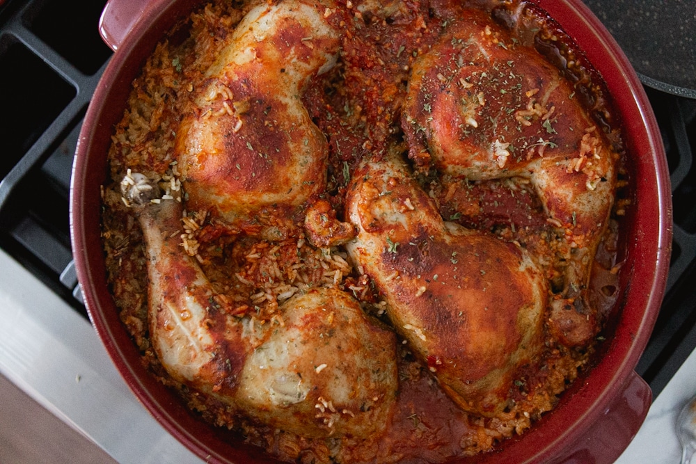 One pot chicken and rice: A red Dutch oven, with red coloured rice and chicken on top.