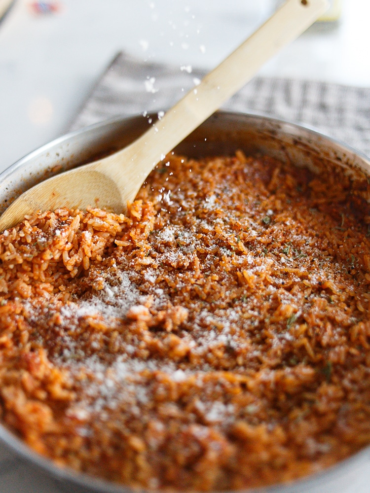 A pan with a wood spoon, inside is tomato rice topped with parsley