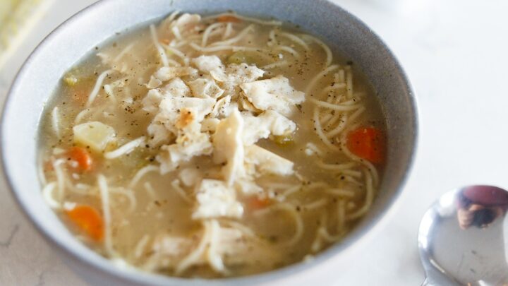 A grey bowl filled with chicken broth, noodles, carrots and other vegetables. Homemade chicken noodle soup.