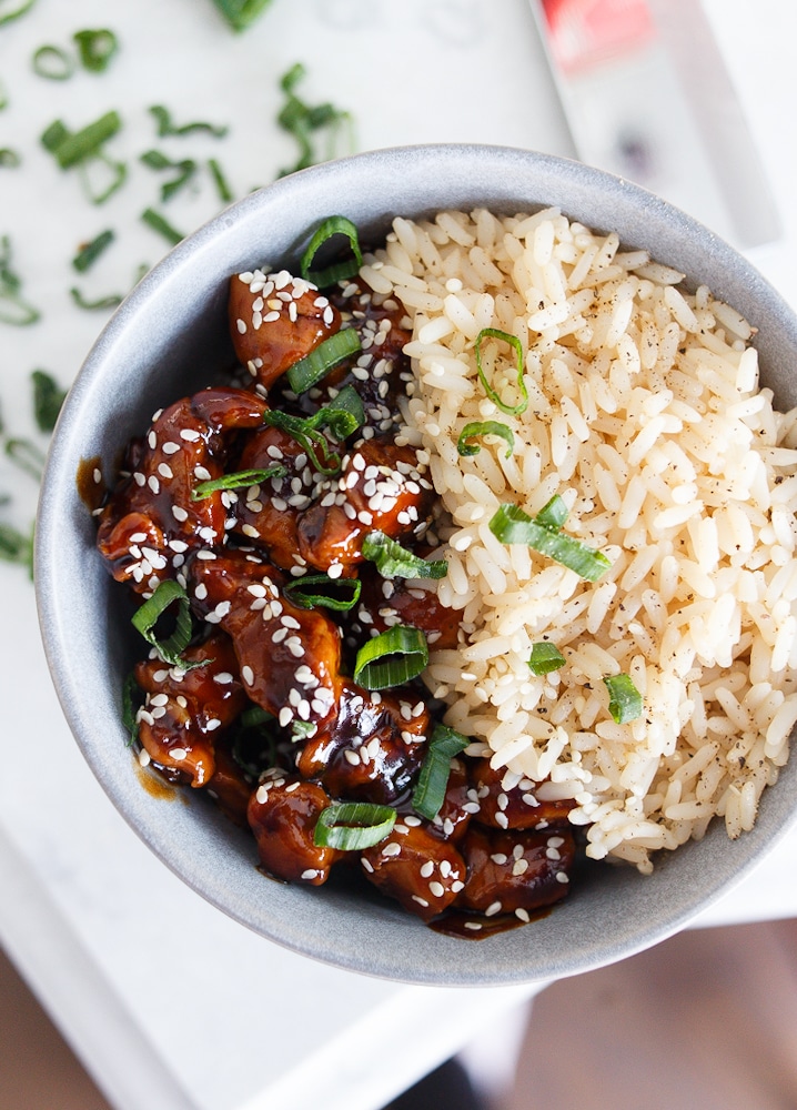 A light blue bowl filled with rice and honey sesame chicken.