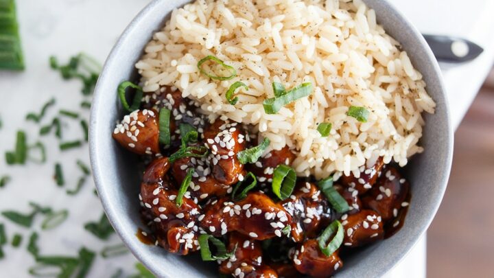 A light blue bowl filled half with rice and the other side with sesame honey chicken